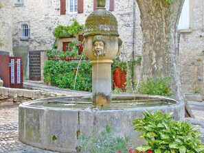 Stunning stone fountain surrounded by lush greenery and a historic stone building.
