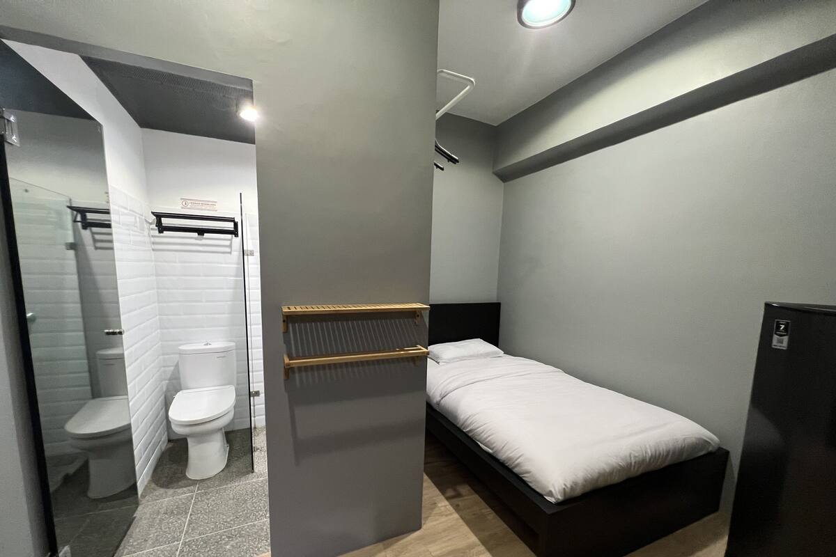 A compact room with a bed, a toilet, and a small refrigerator.