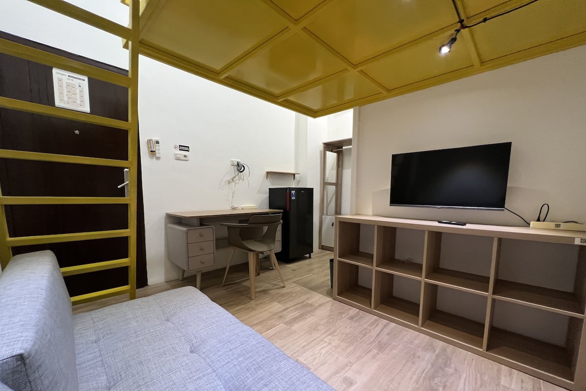 A compact room with a bed, a desk, a chair, a TV, and a wardrobe.