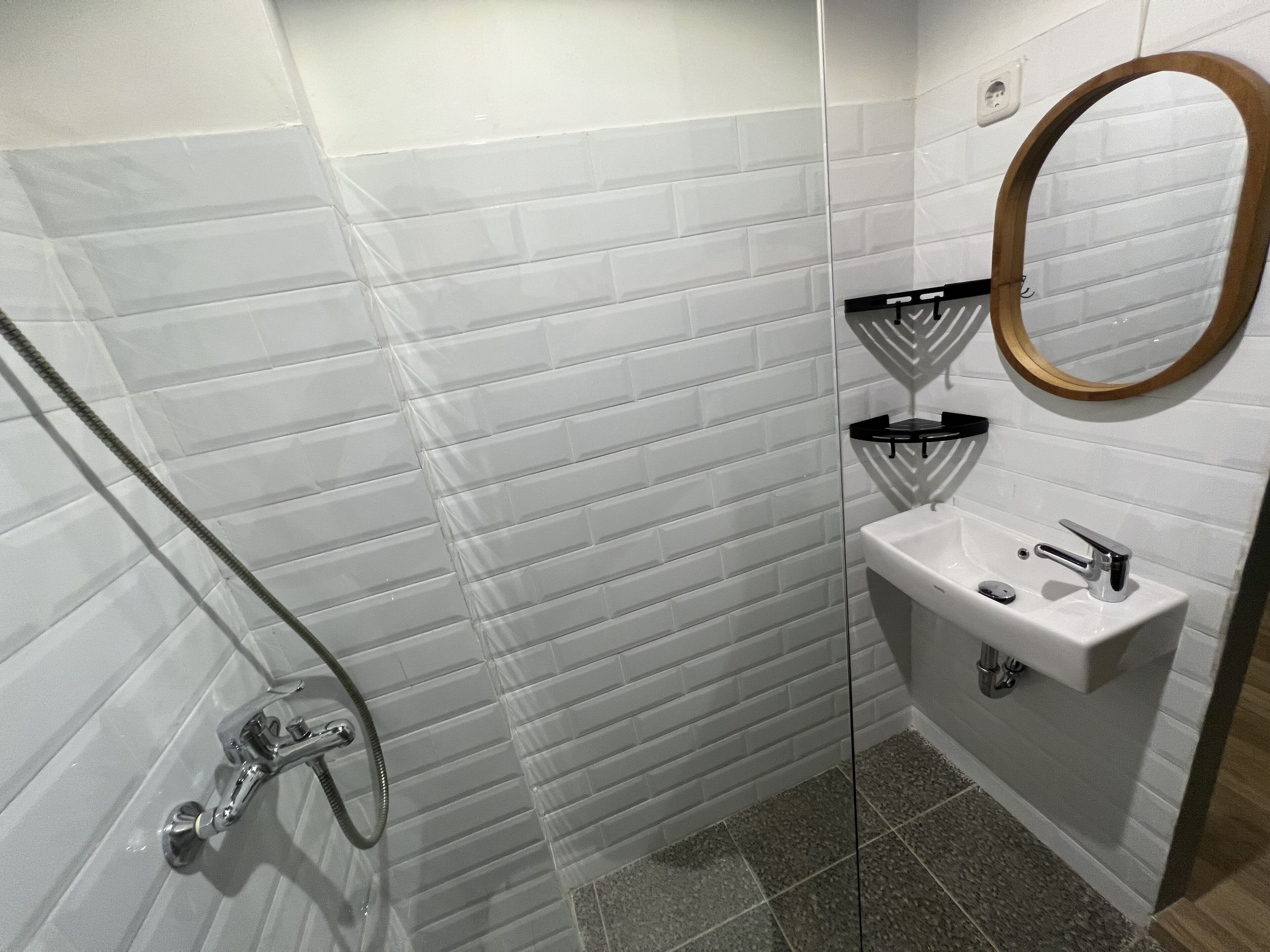 A small bathroom with white subway tiles, a glass shower enclosure, a sink with a mirror, and a black towel rack.