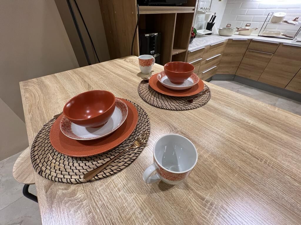 A wooden dining table with a red and white set of bowls and a matching cup, accompanied by a woven placemat.