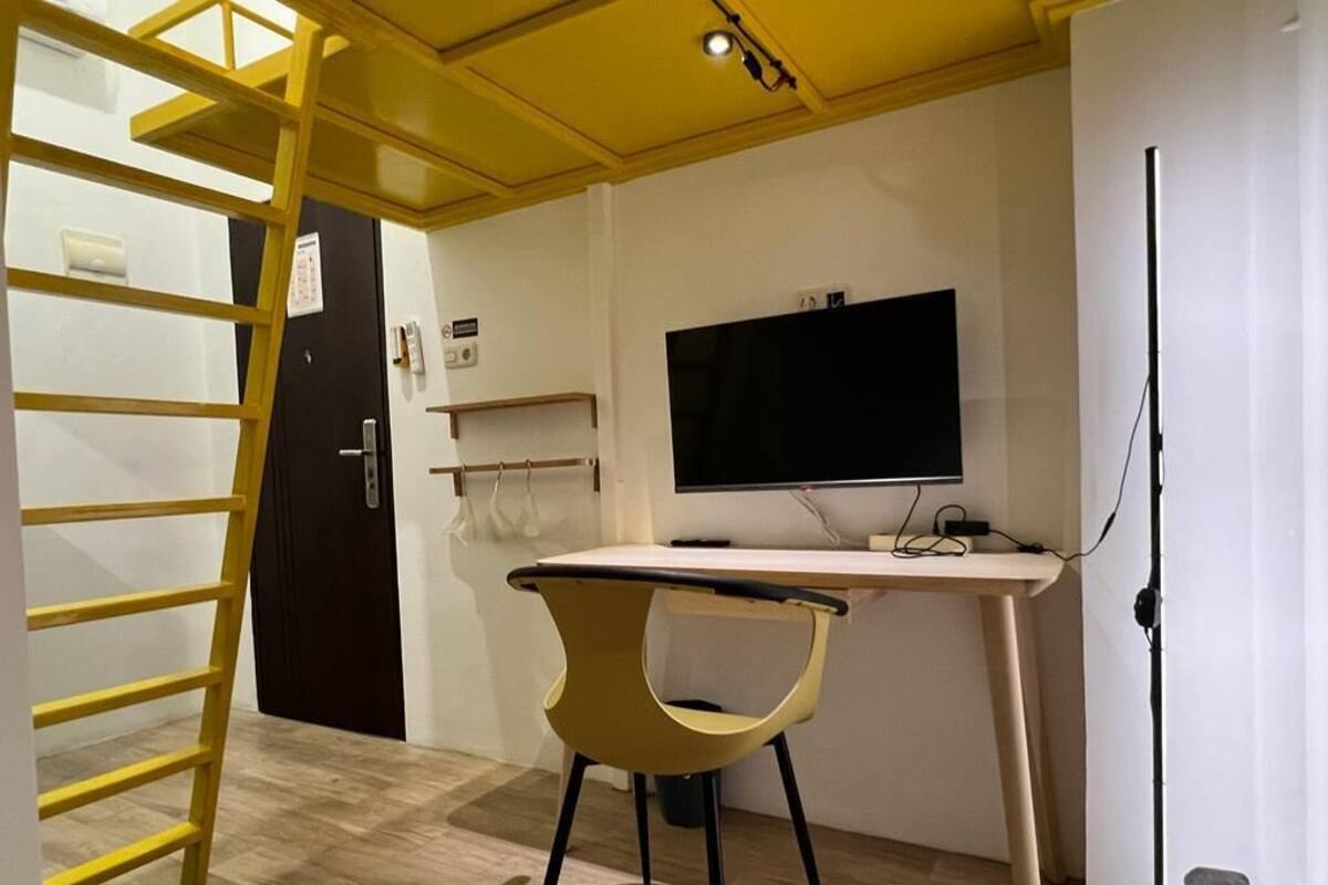 A room with a desk, chair, TV, and a ladder.
