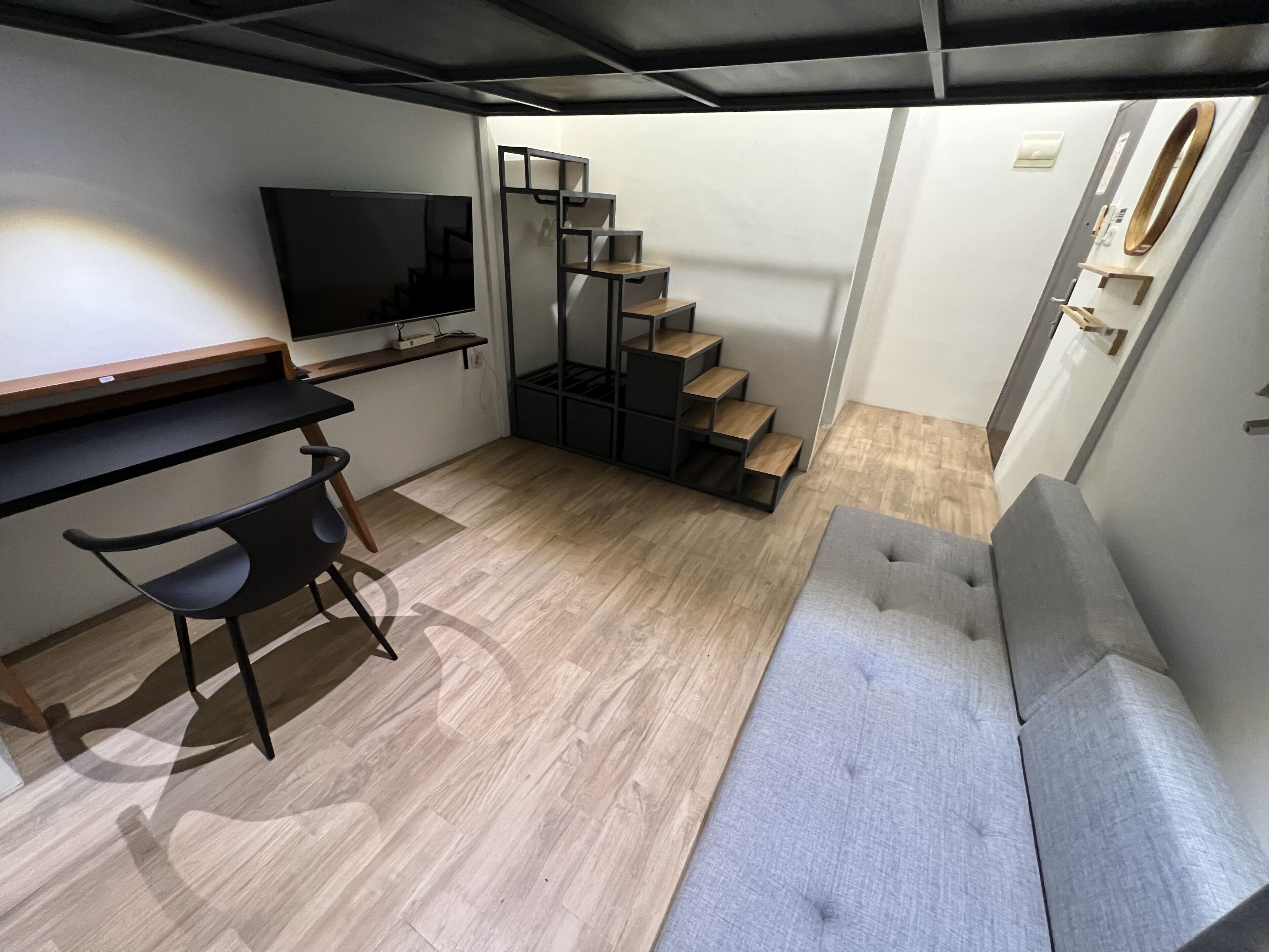 Ett kompakt bostadsutrymme med en soffa, en tv, ett skrivbord med en stol och en trappa.