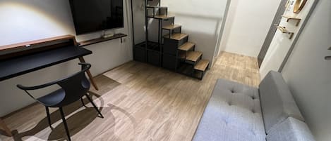 Ett kompakt bostadsutrymme med en soffa, en tv, ett skrivbord med en stol och en trappa.