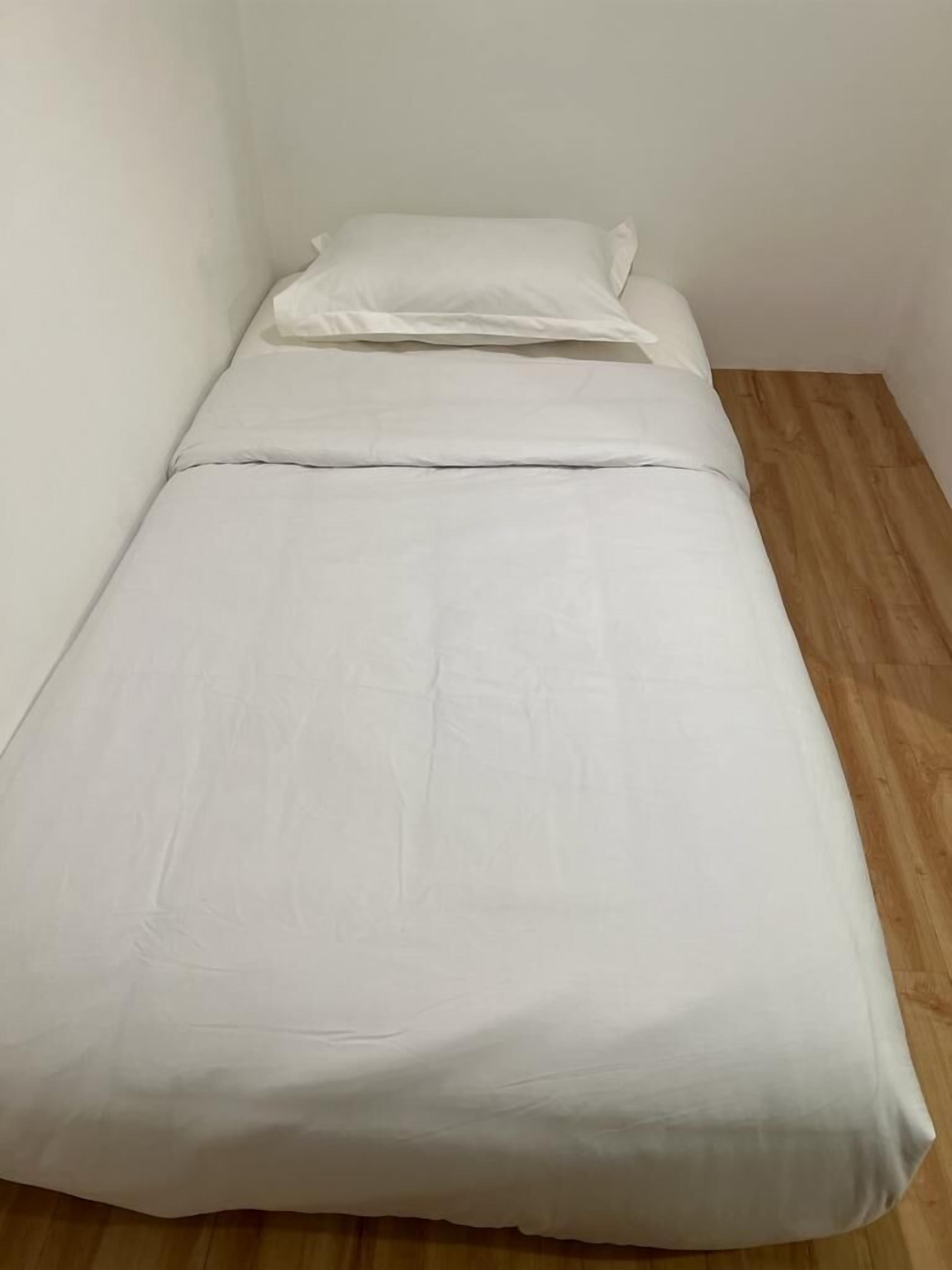 A small, single-bed room with a wooden floor and white bedding.