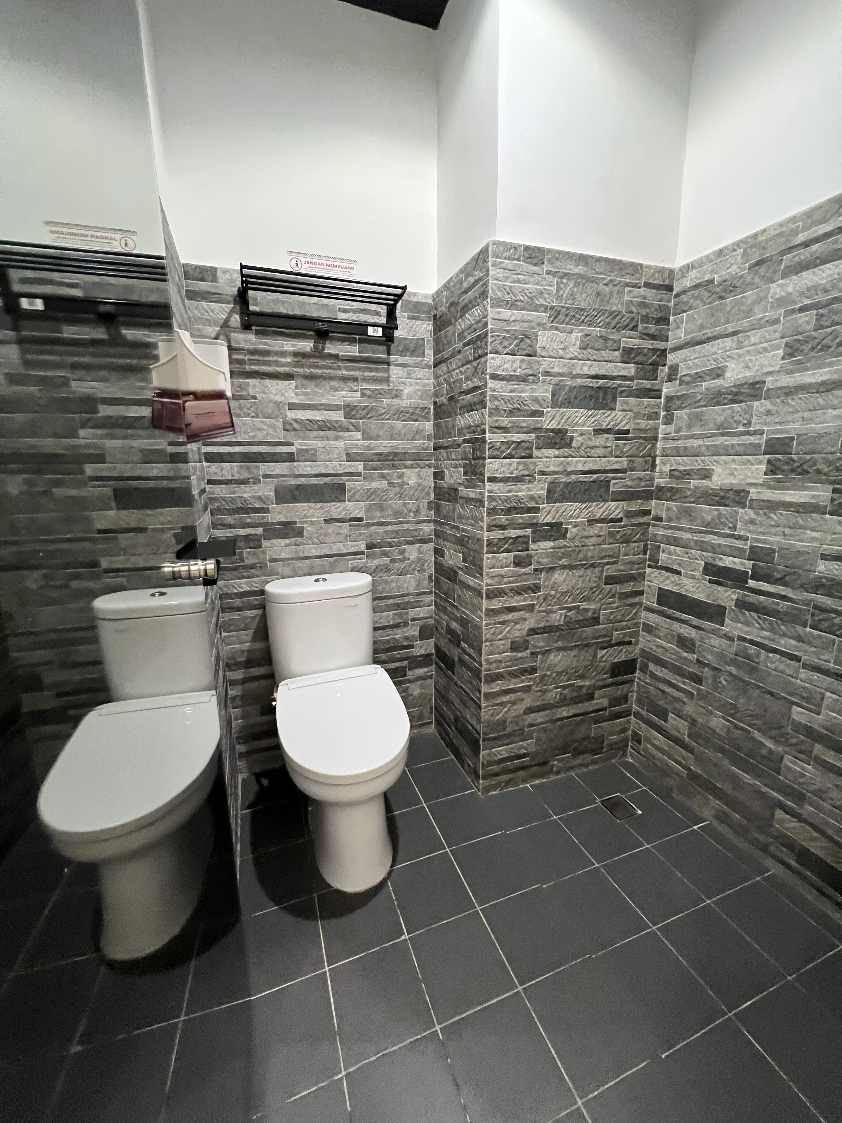 Un baño con dos inodoros, zona de ducha y suelo de baldosas.