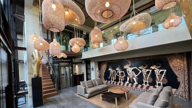 A spacious lobby with a modern sofa set, a large woven light fixture, and a mural with animal figures.