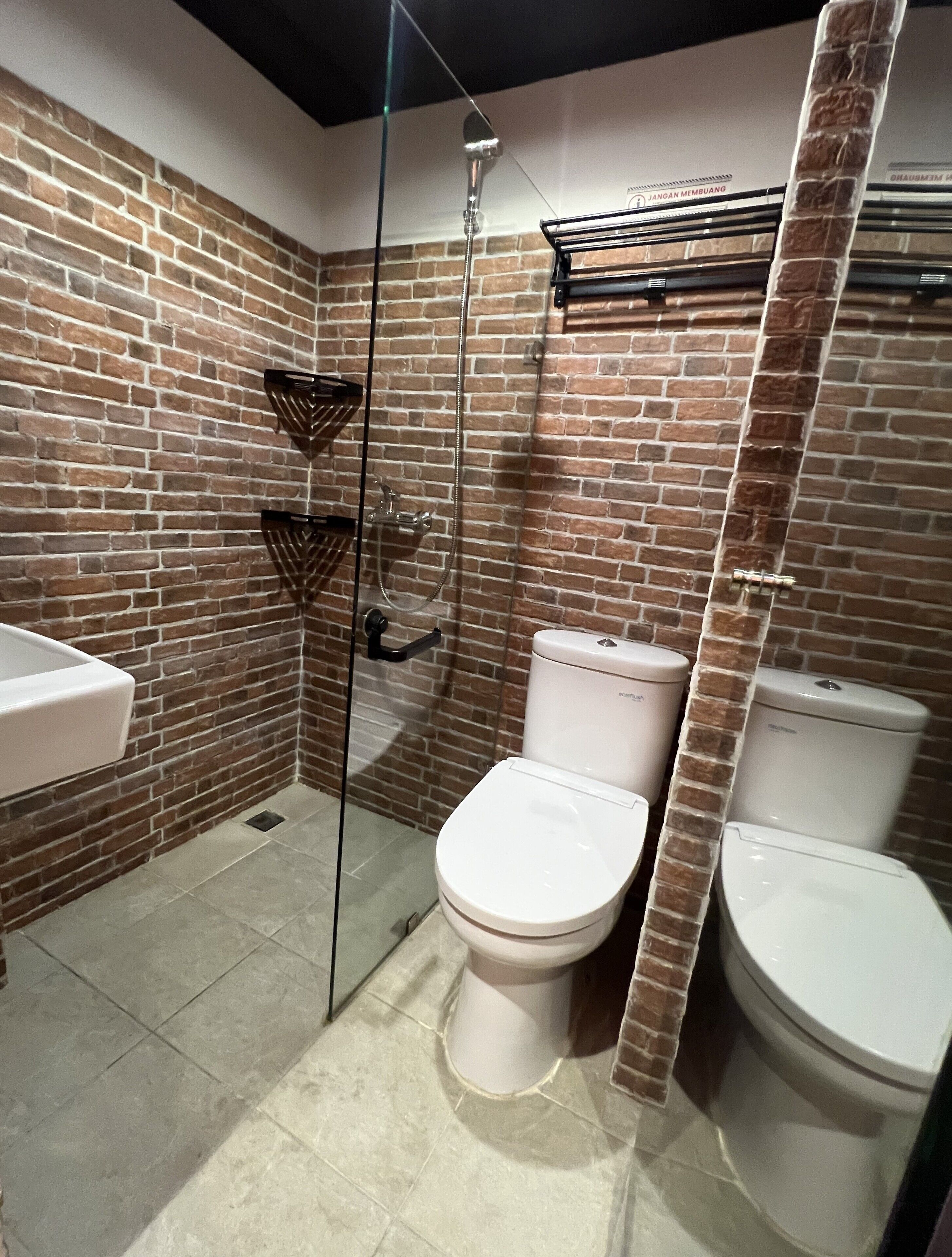 Un baño con pared de ladrillo, cabina de ducha de vidrio y dos inodoros.