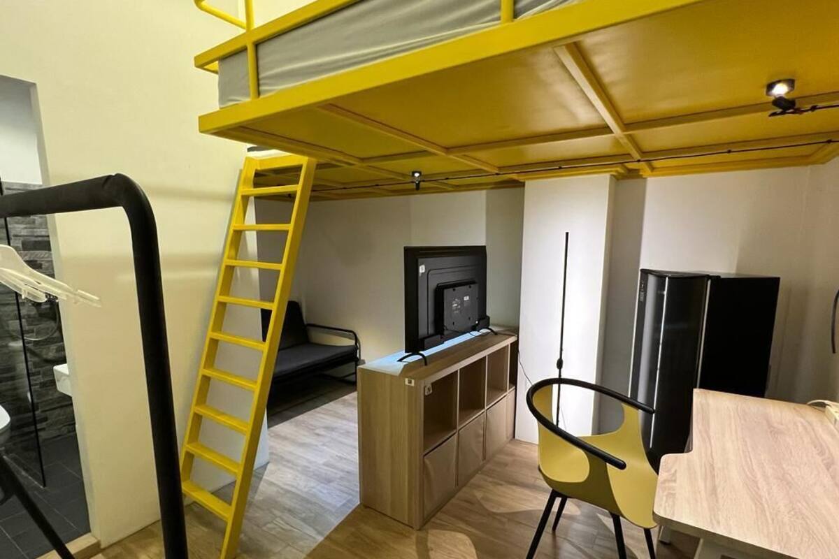 A compact room with a bunk bed, a small TV, a desk, and a chair.