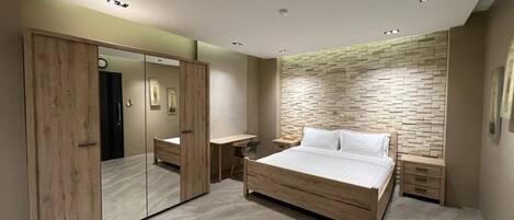 A modern bedroom with a large bed, a wardrobe with a mirror, and a nightstand.
