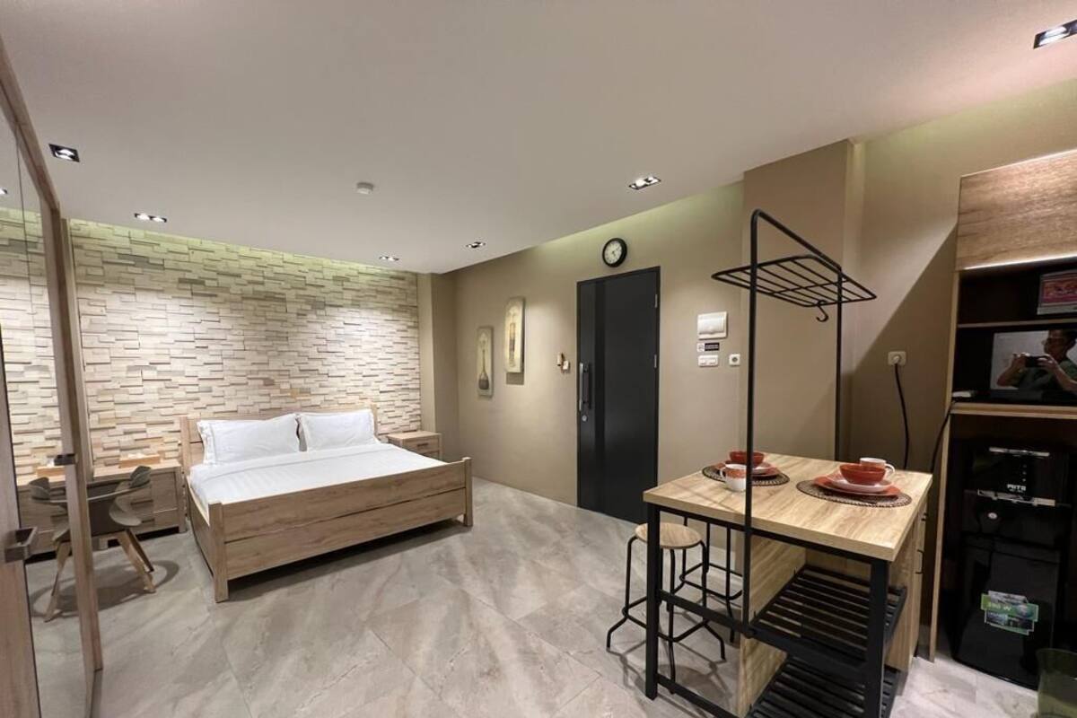 A compact room with a bed, a small table with chairs, a coffee machine, and a wall-mounted shelf.
