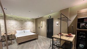 A compact room with a bed, a small table with chairs, a coffee machine, and a wall-mounted shelf.
