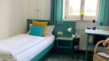 A small, neatly arranged room with a single bed, a desk, and a chair.