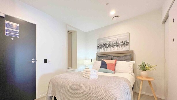 Ein Schlafzimmer mit einem Bett, einem Nachttisch, einem an der Wand befestigten Kunstwerk und einer Tür.