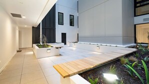 Ein moderner Innenhof mit Holzdeck, Pflanzgefäßen und einem Wasserspiel.