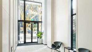 Eine moderne Lobby mit Glastür, einer Zimmerpflanze und zwei Stühlen.