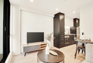 A modern living room with a flat-screen TV, a round coffee table, and a dining area with a table and chairs.