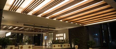 A modern building with a wooden slatted ceiling, a reception area with a digital screen, and potted plants.