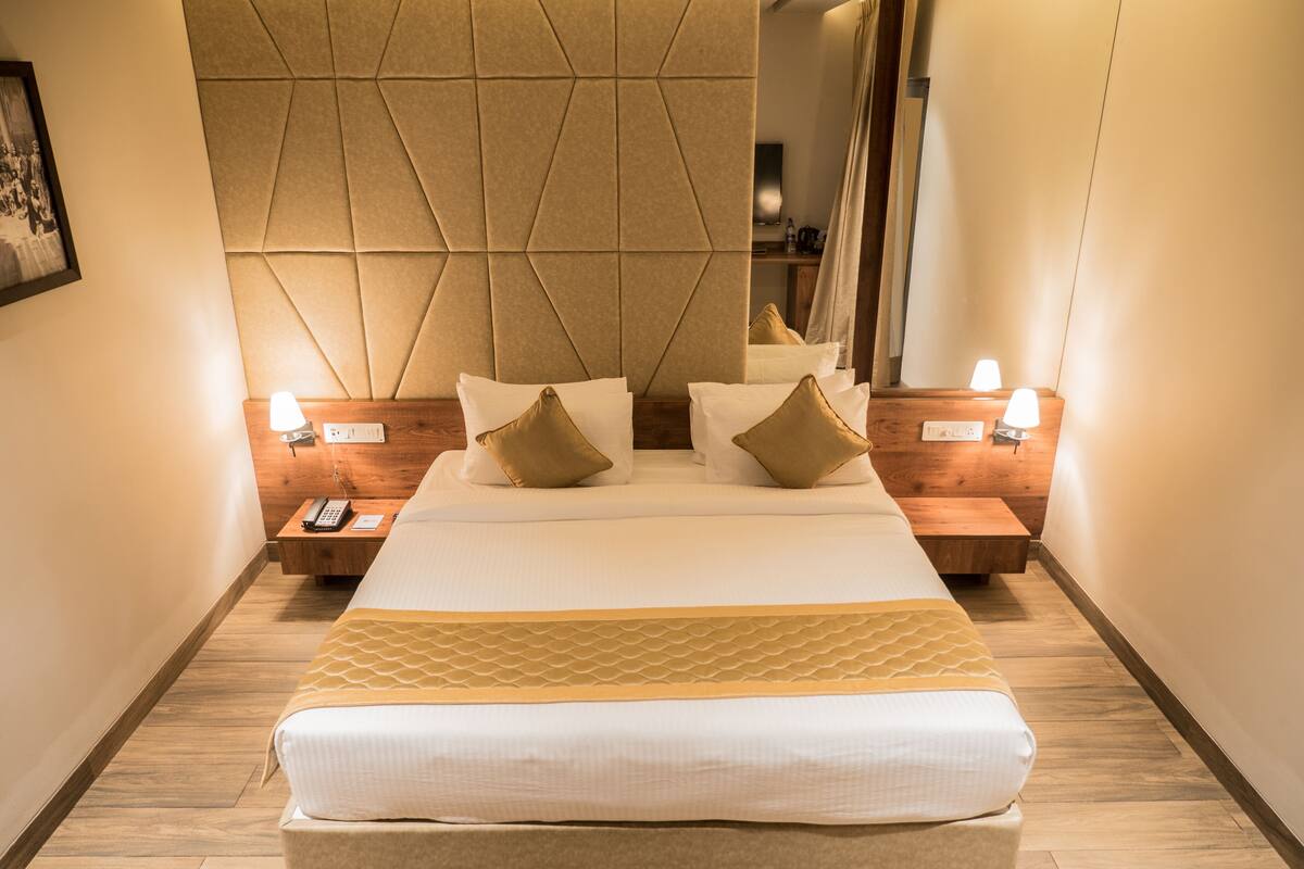 Une chambre d’hôtel avec un grand lit, deux tables de chevet, une commode, un miroir et un téléviseur fixé au mur.