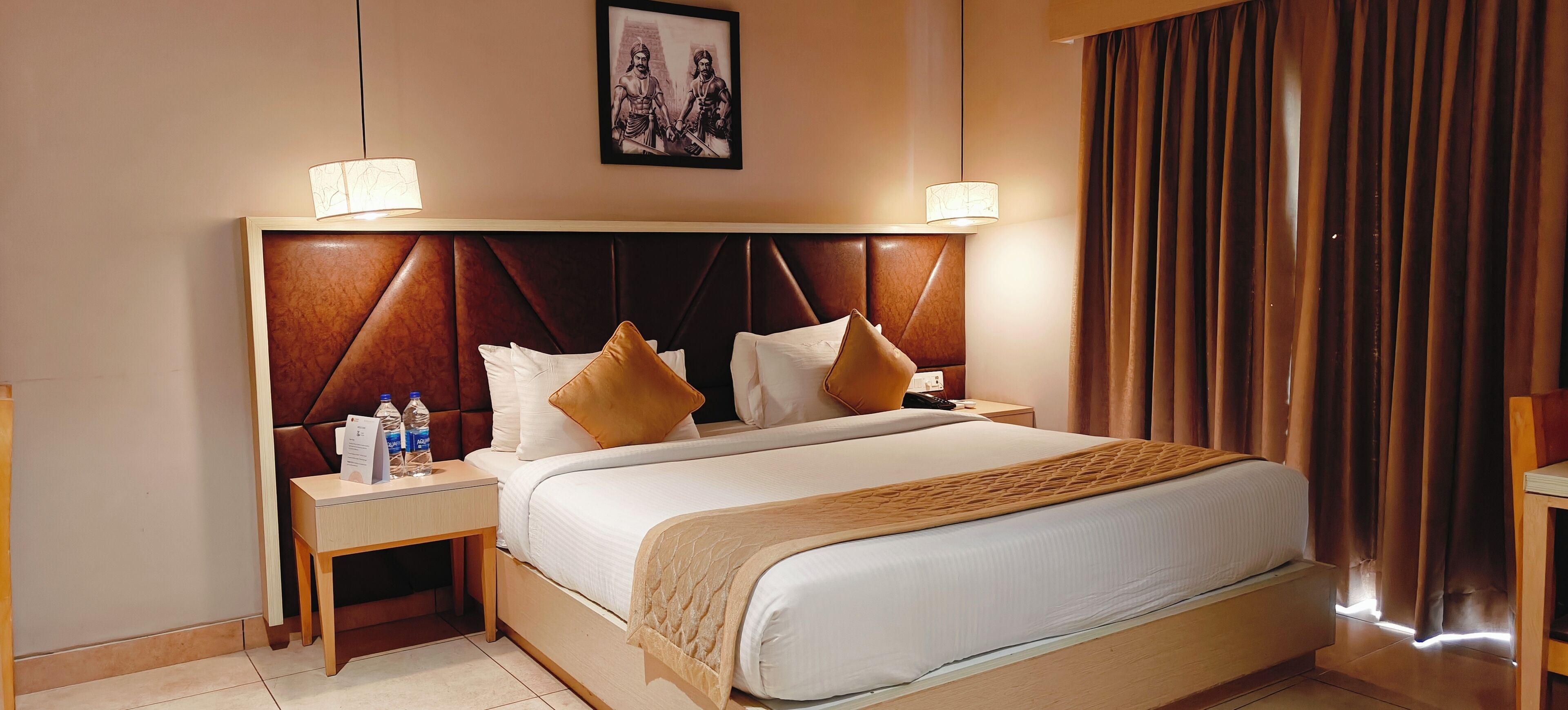 A hotel room with a large bed, two bedside tables, a headboard, and a framed picture on the wall.