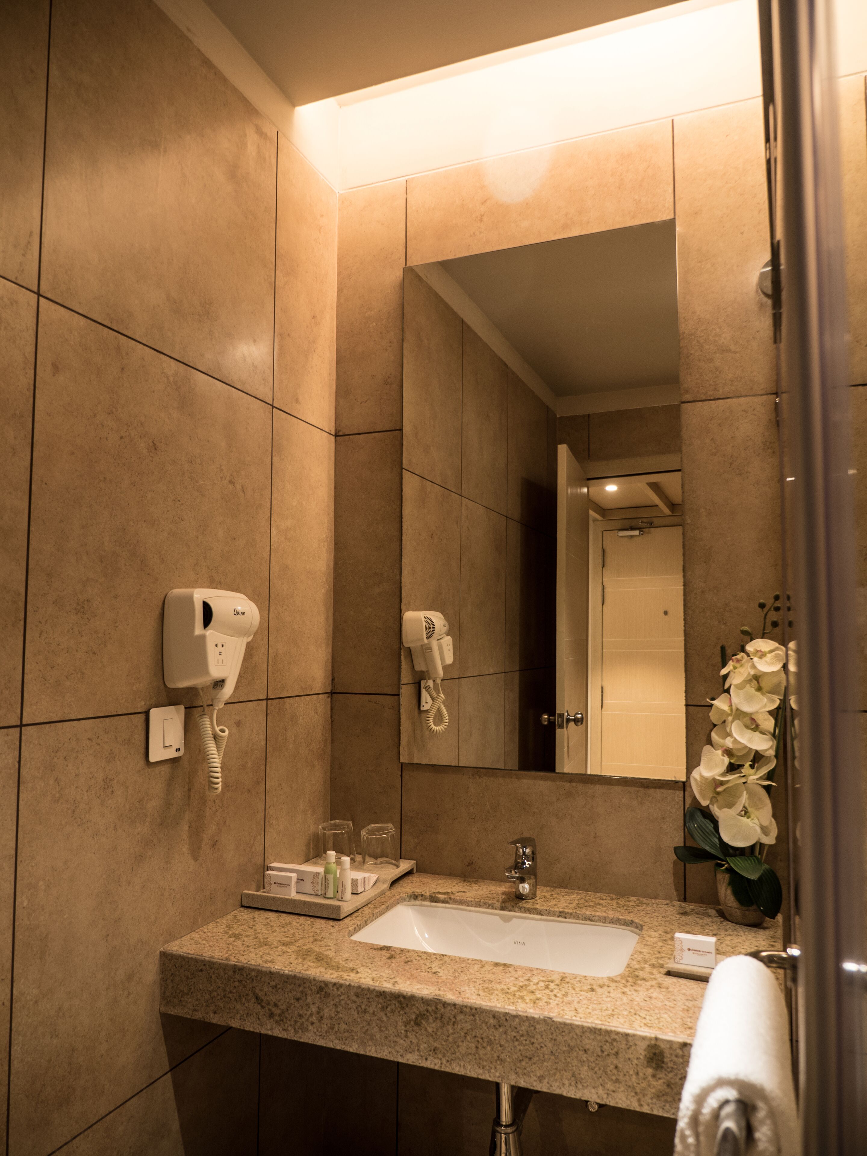 A modern bathroom with a granite countertop, a sink, a mirror, and two hair dryers mounted on the wall.