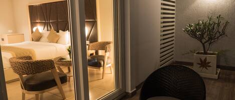 A modern hotel room with a bed, two chairs, a small table, and a potted plant.