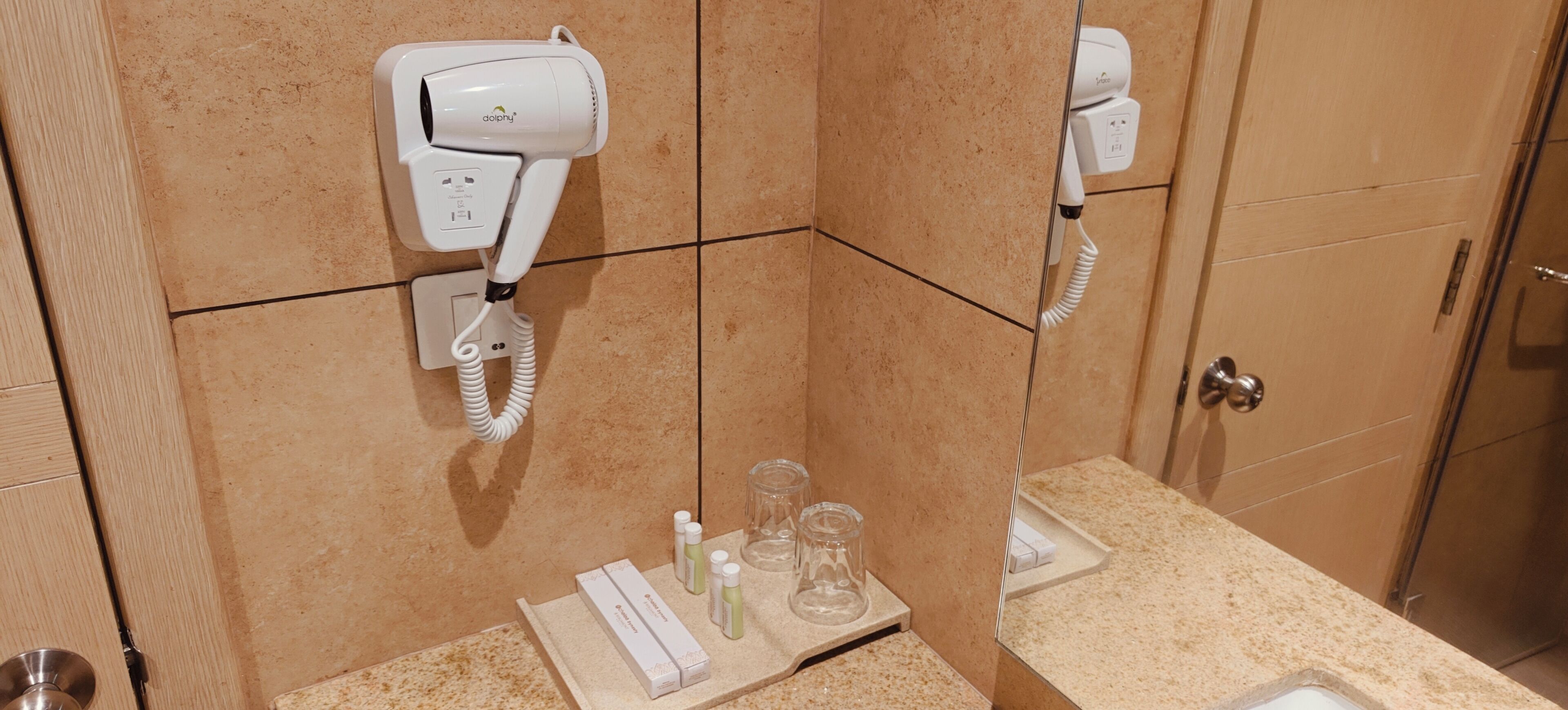 A bathroom with a hairdryer mounted on the wall, a towel rack, and a shelf with toiletries.