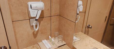 A bathroom with a hairdryer mounted on the wall, a towel rack, and a shelf with toiletries.