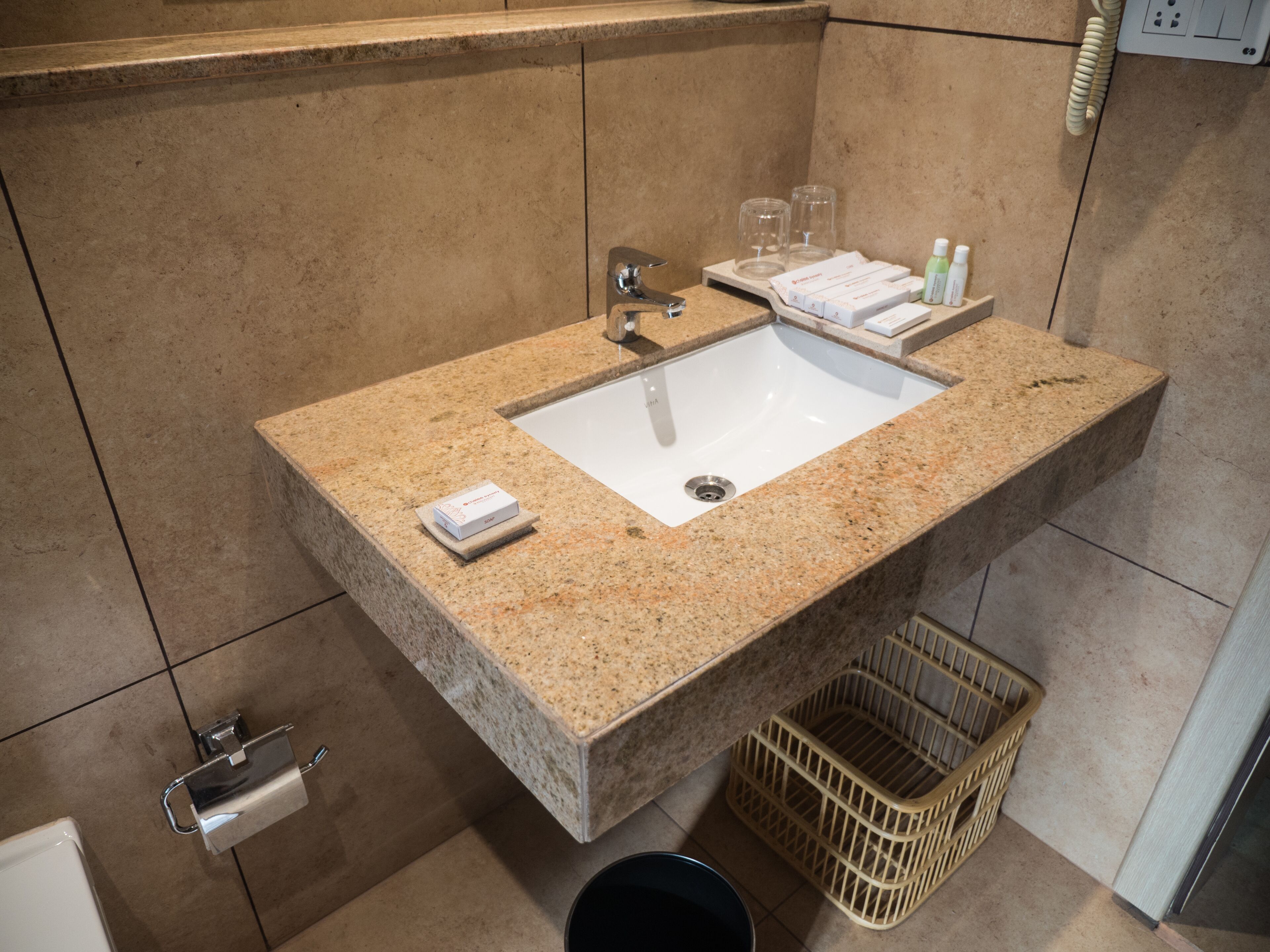 A bathroom with a granite sink, a towel rack, a basket, and toiletries.