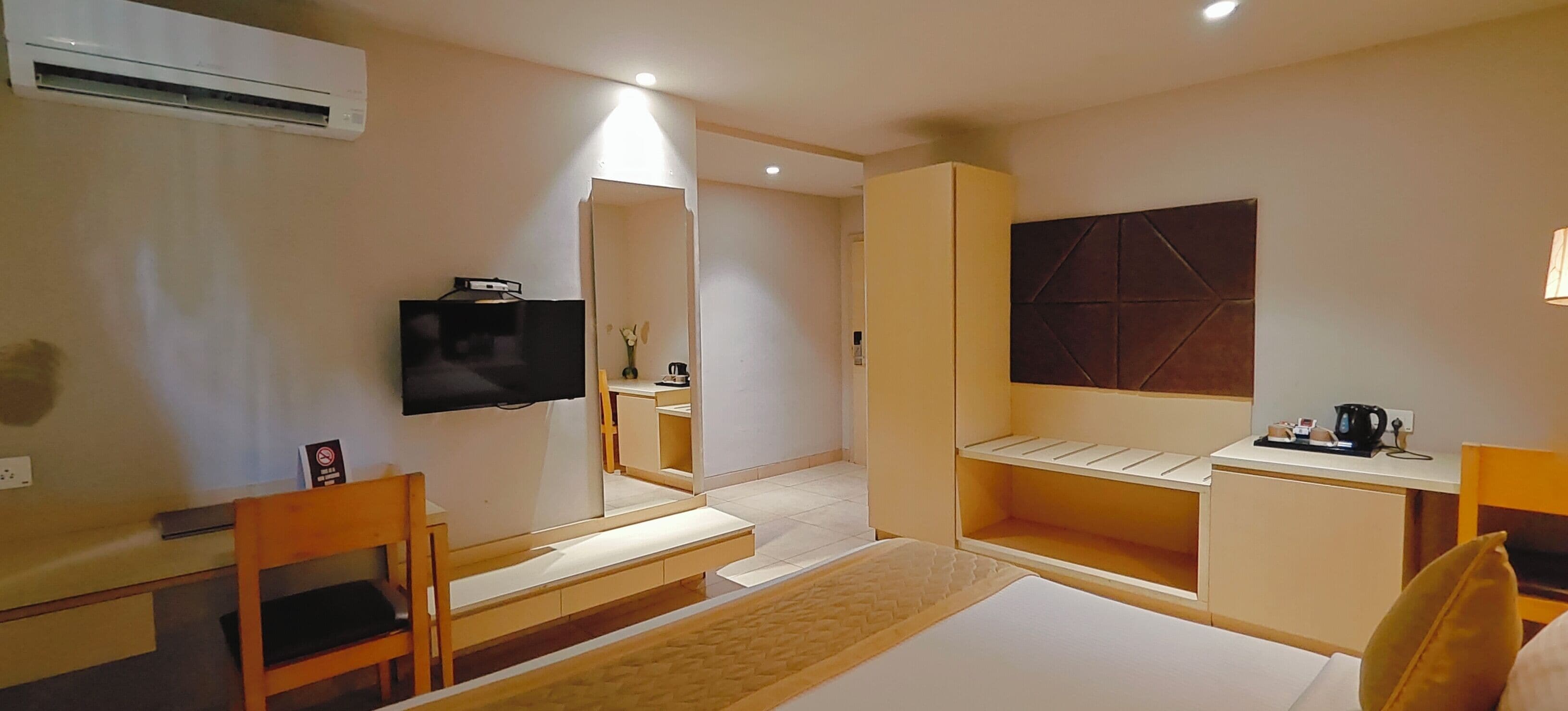 A hotel room with a bed, a desk, a chair, a television, and a mirror.