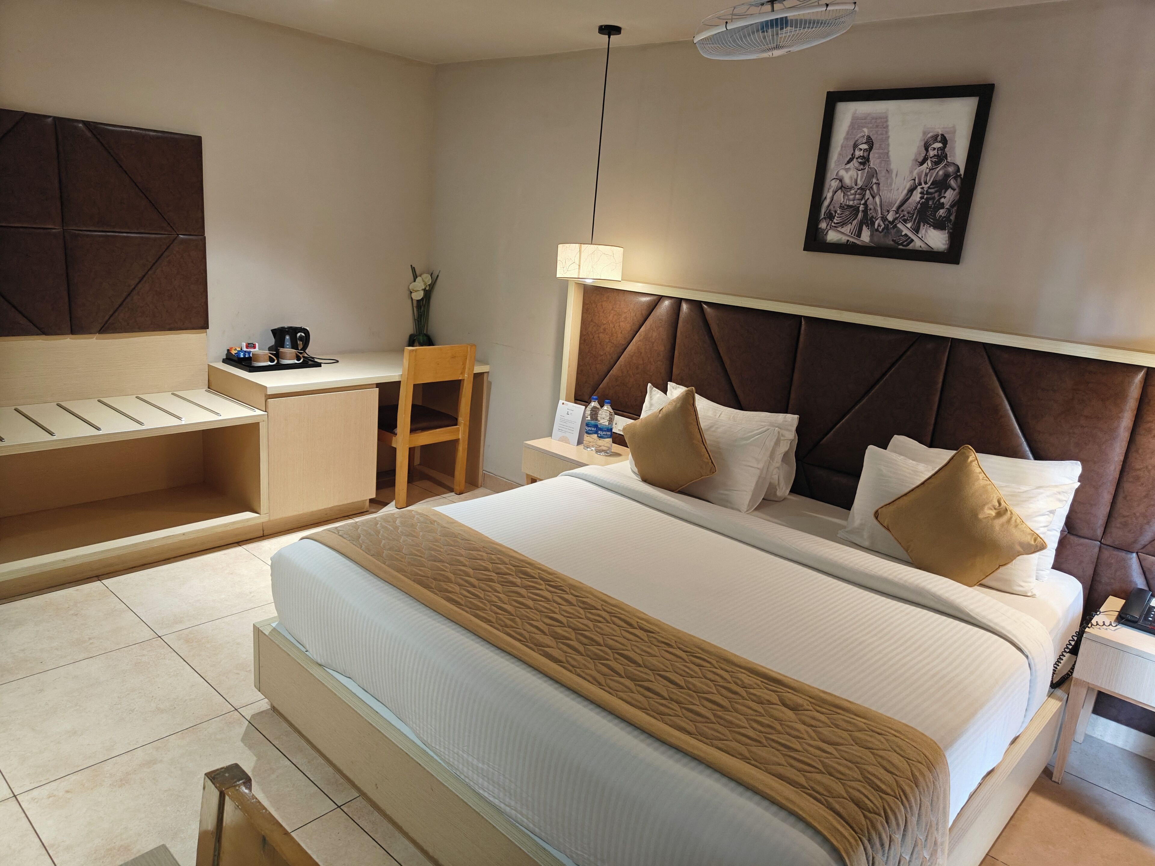 A hotel room with a bed, desk, chair, and a framed picture on the wall.