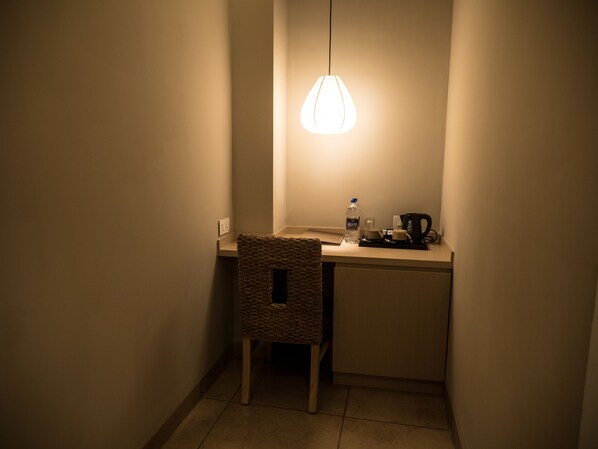 A small, dimly lit room with a single chair, a table with a water bottle, a glass, and a coffee maker.