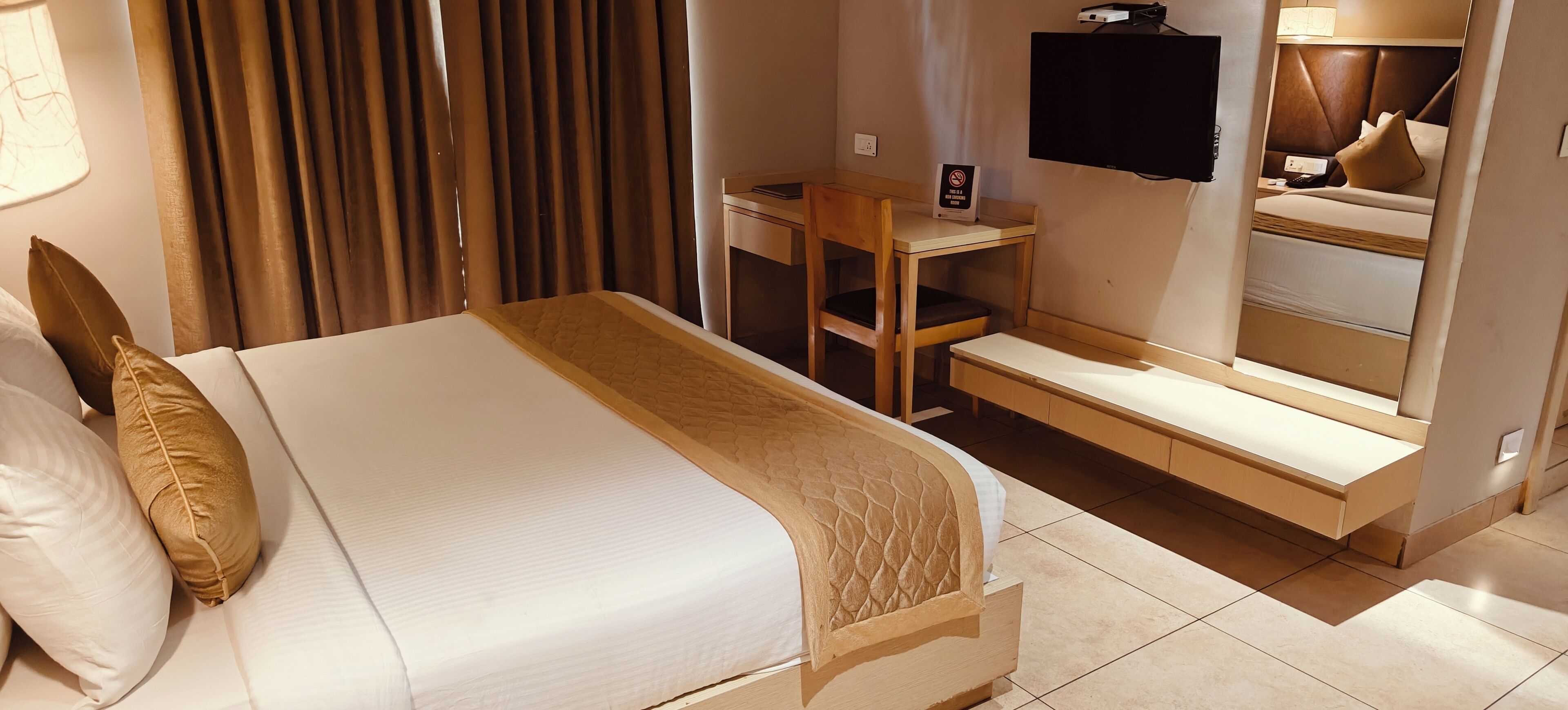 Una habitación de hotel con cama, escritorio, silla, televisor y espejo.