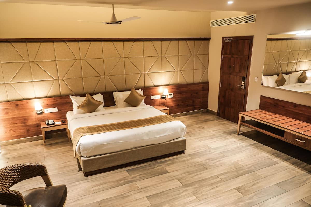 Une chambre d’hôtel moderne avec un grand lit, des tables de chevet, un banc en bois et une tête de lit fixée au mur.
