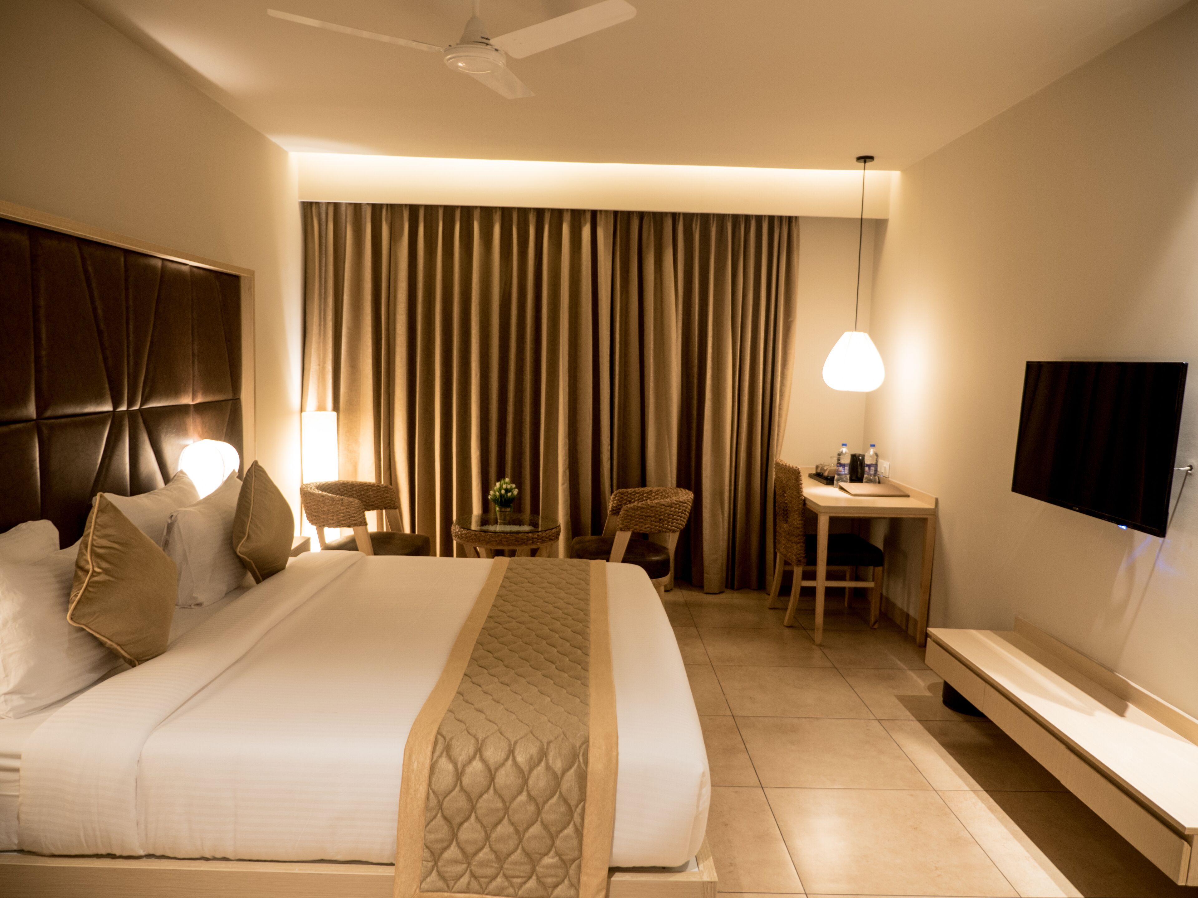 Een hotelkamer met een groot bed, een bureau, een stoel, een televisie en een plafondventilator.