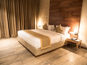 A modern hotel room with a large bed, wooden headboard, and a nightstand with a phone and lamp.