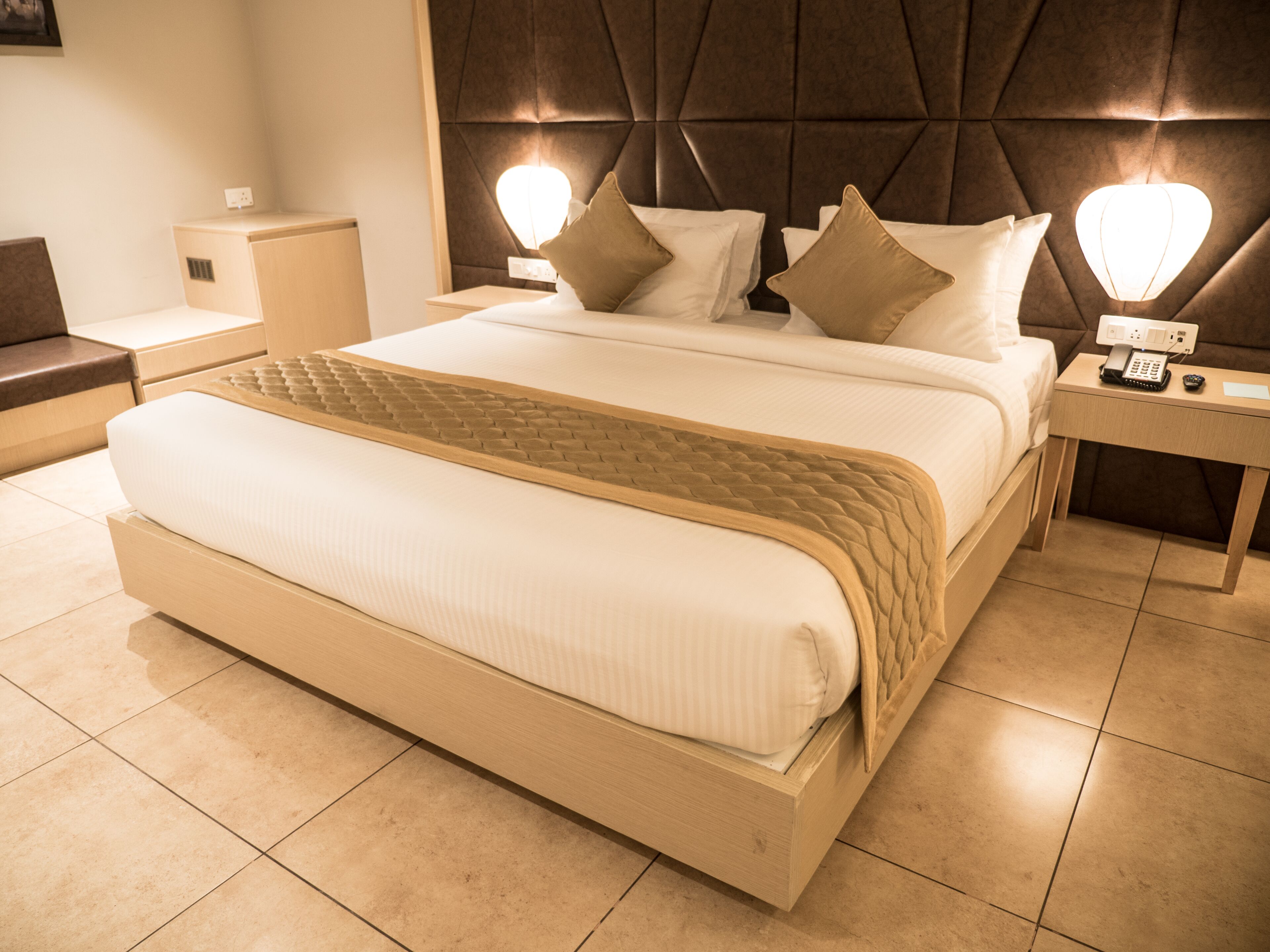 A large bed with a headboard, two bedside tables, and a nightstand with a phone and a lamp.