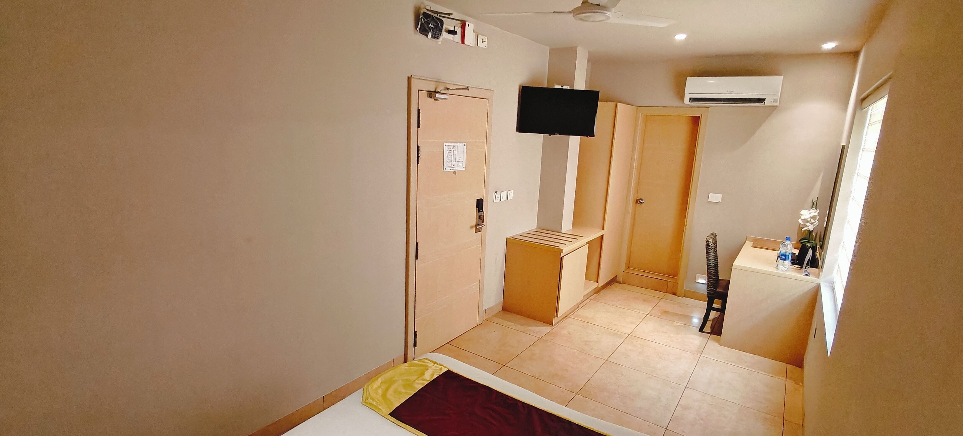 A hotel room with a bed, a desk, a chair, a television, and an air conditioning unit.