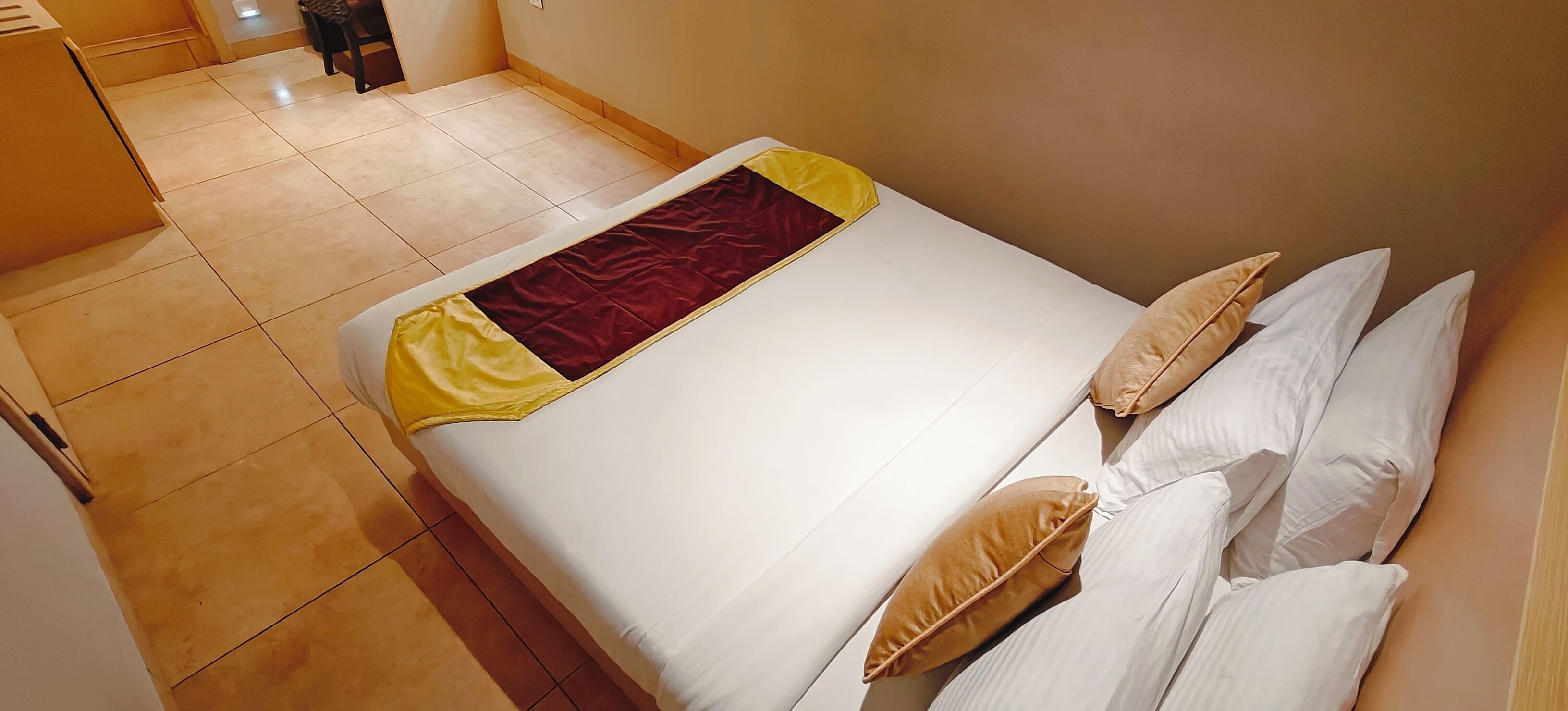 A hotel room with a bed, pillows, and a tiled floor.