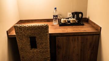 Un rincón pequeño y acogedor con un escritorio de madera, una silla tejida, una botella de agua, una cafetera y un cubo de basura.