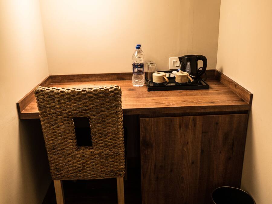 Un rincón pequeño y acogedor con un escritorio de madera, una silla tejida, una botella de agua, una cafetera y un cubo de basura.