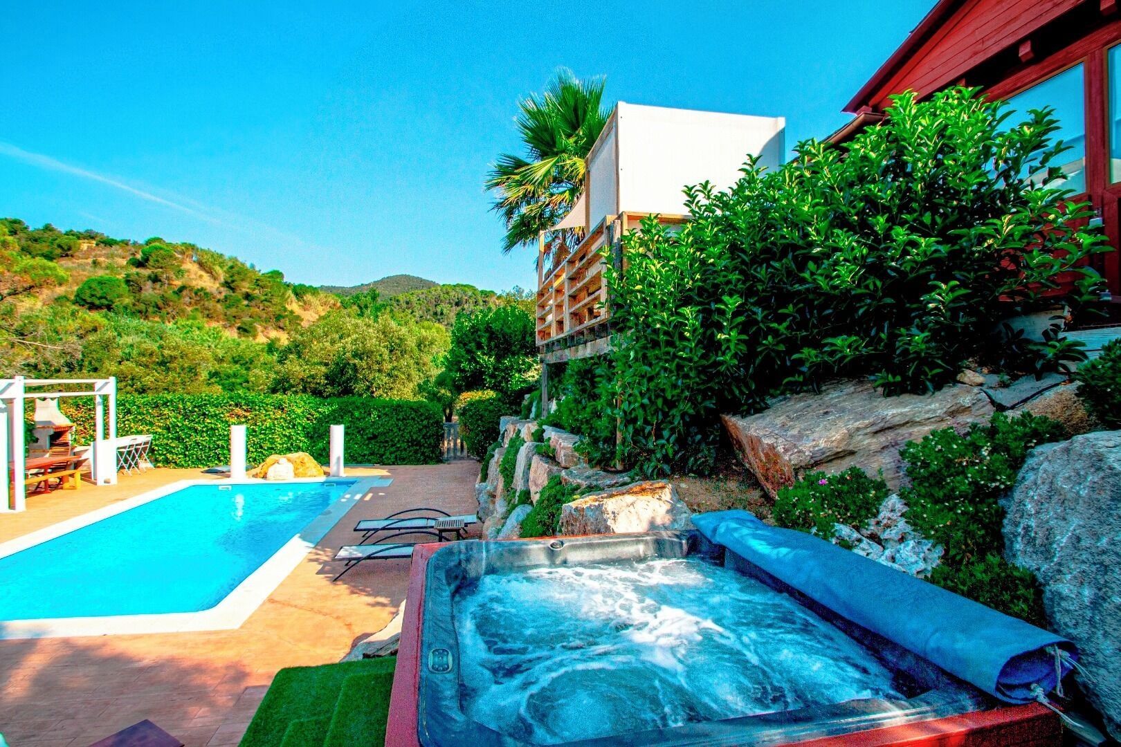A swimming pool with a hot tub, lounge chairs, and a view of a hillside.