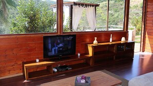 A wooden interior with a television, wooden benches, and a view of greenery outside. - Club Villamar - Rent your dream villa and spend an unforgettable holiday (Calonge)