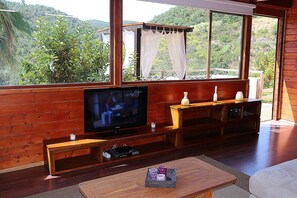 Ein Holzinterieur mit Fernseher, hölzernen Bänken und Blick auf Grünflächen außerhalb.