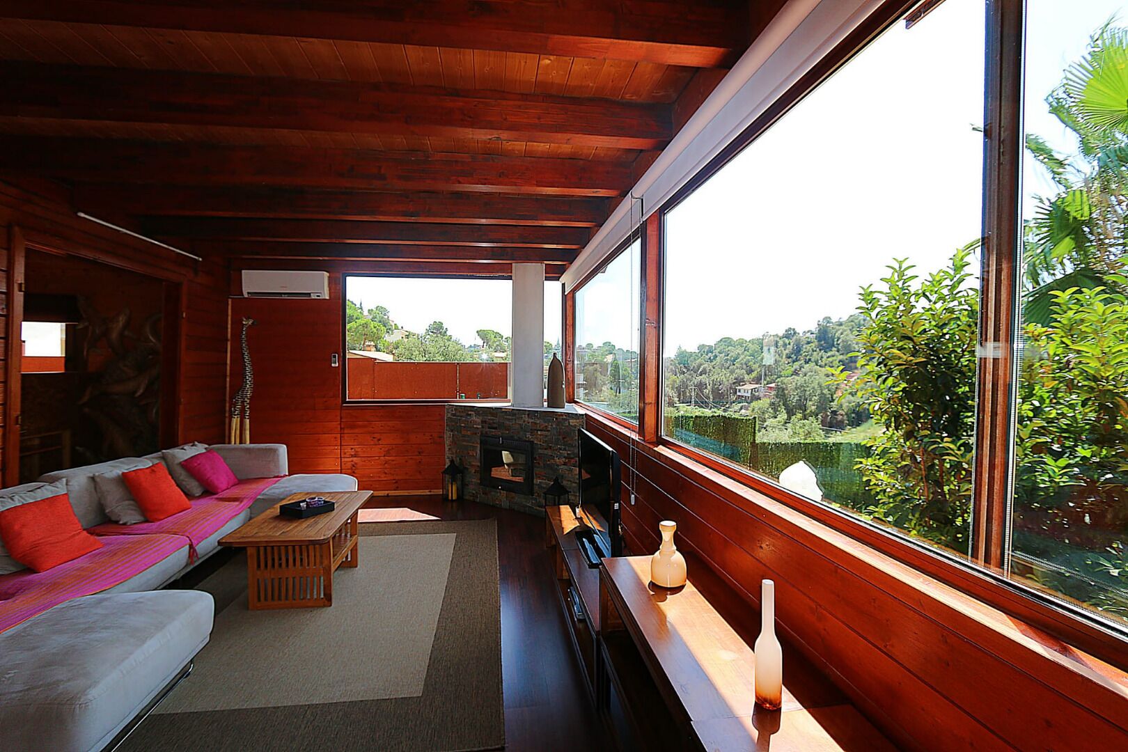 Un salon chaleureux avec un canapé, une table basse et une cheminée, de grandes fenêtres offrant une vue sur la verdure.