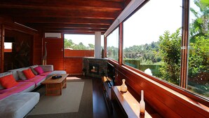 A cozy living room with a sofa, coffee table, and fireplace, large windows offering a view of greenery. - Club Villamar - Rent your dream villa and spend an unforgettable holiday (Calonge)