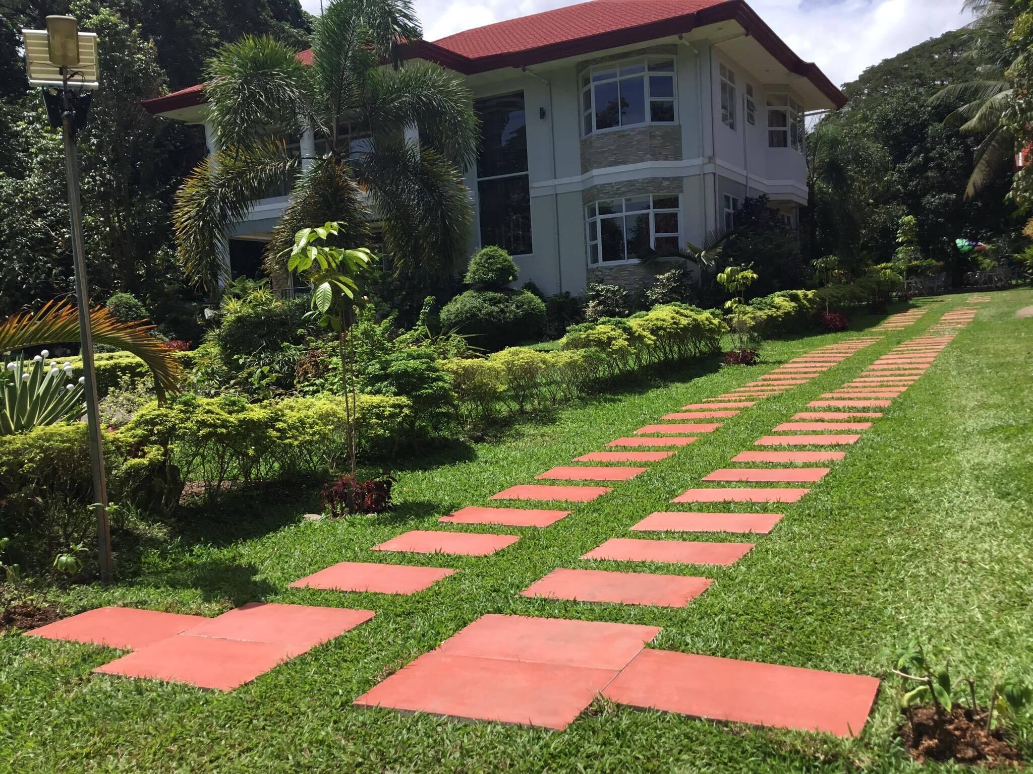 A well-maintained garden with a red pathway leading to a two-story building with a red roof.