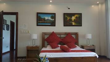 A hotel room with a wooden bed, red pillows, two bedside tables with lamps, and two framed landscape paintings on the wall.