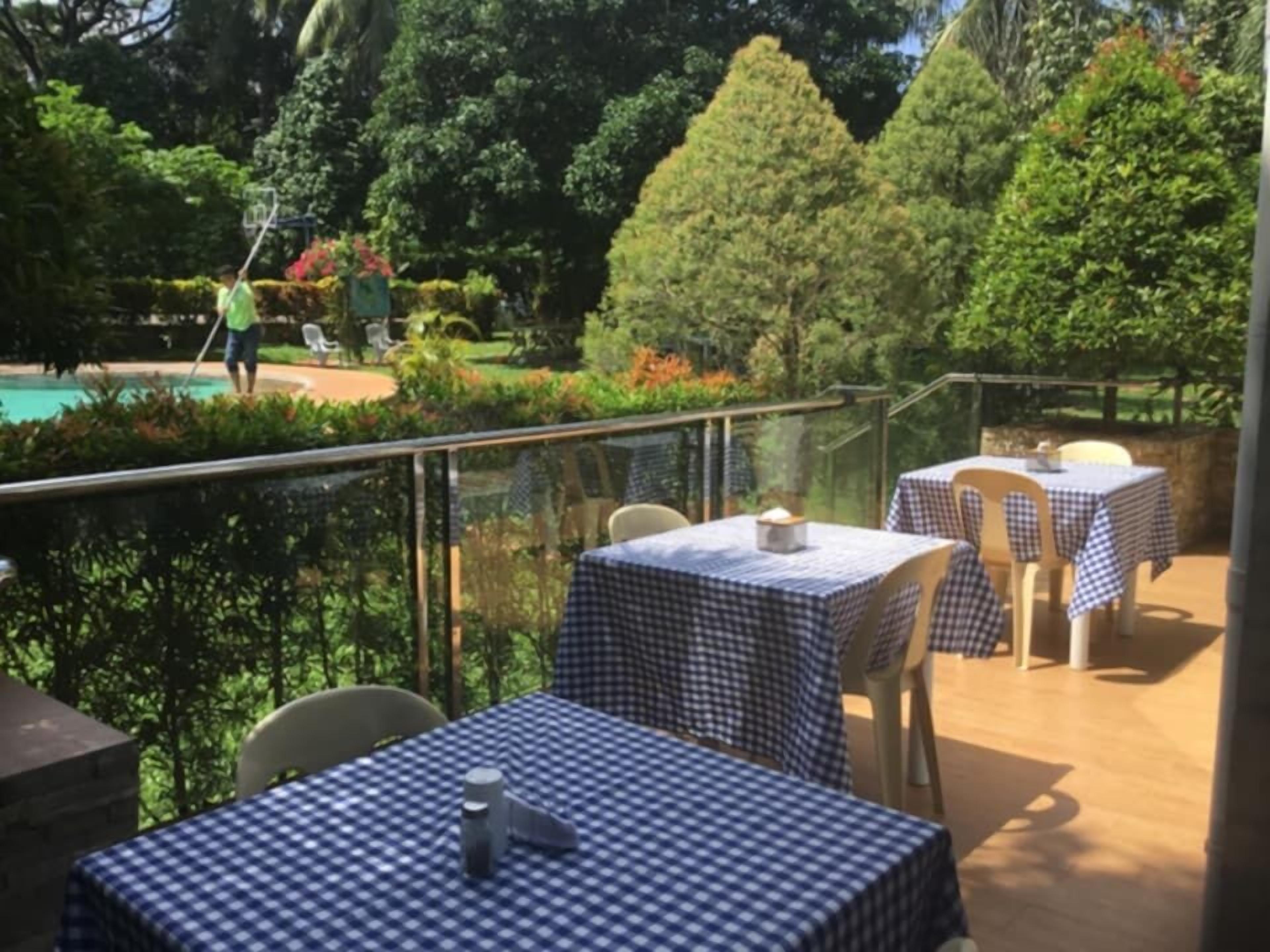 Un espace extérieur aménagé pour les repas, avec des tables recouvertes de nappes à carreaux et des chaises, offrant une vue sur une piscine et une végétation luxuriante.