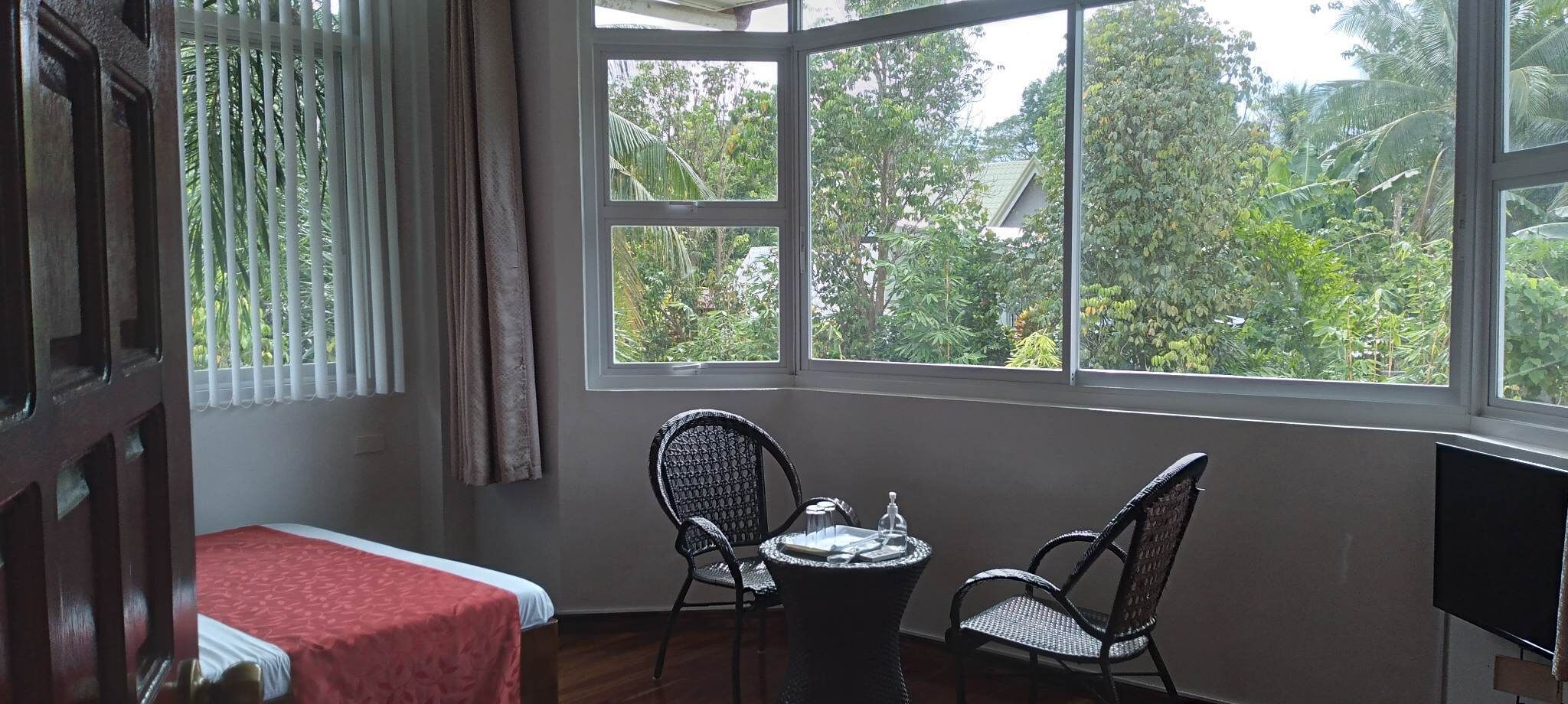 A room with a bed, two wicker chairs, a small table, and a TV.